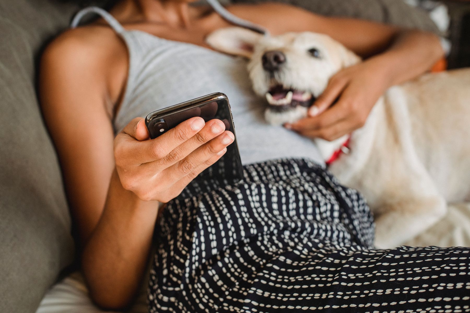 A pet owner holding a phone while relaxing with a dog